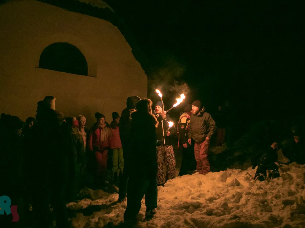Fackelträger stehen abends vor einem Gebäude.